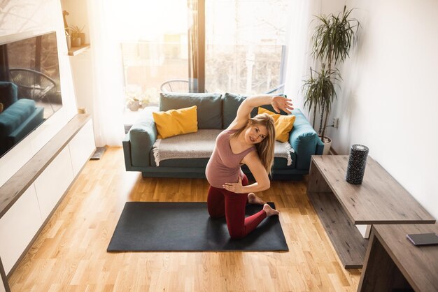 A pregnant woman in sports clothing is stretching and exercising to promote wellbeing in her living room.