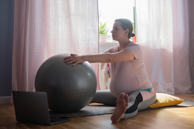 Pregnant woman in sportswear, doing yoga, pilates training, Wide Angle Seated Forward Bend pose, Upavishtha Konasana at home