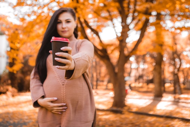 Pregnant woman standing in autumn city park forest, stroking her round belly with baby child inside