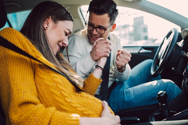 Pregnant woman starting to feel pain and contractions while her worried husband driving a car.