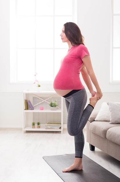 Pregnant woman stretching legs training at home. Expectant female makes warmup aerobics exercise, healthy pregnancy concept