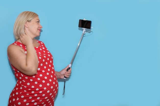 Pregnant woman taking selfie on blue background with copy space