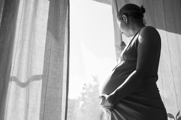 Pregnant woman touching belly standing near window