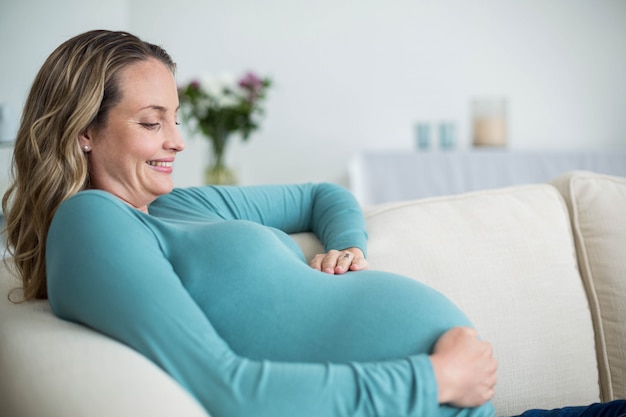 Pregnant woman touching her belly lying on the couch