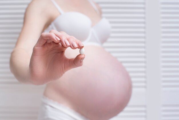 Pregnant woman in underwear holding a pill in her hand on a light 