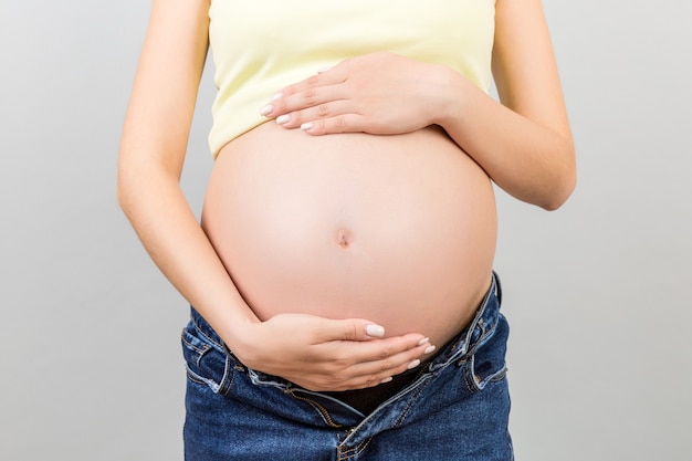 pregnant woman in unzipped jeans showing her baby bump