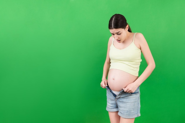 pregnant woman in unzipped jeans showing her naked belly at colorful background with copy space Baby expecting concept