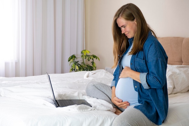 Pregnant woman use her laptop in bed at home browsing surfing net do online shopping reading maternity blogs or chatting online Pregnancy and technology