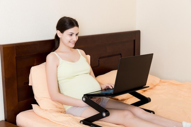 Pregnant Woman Using Laptop Computer in home on bed Pregnant morning work concept