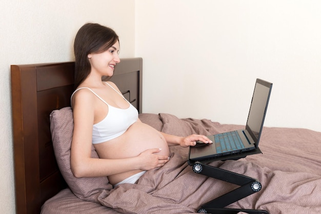 Pregnant Woman Using Laptop Computer in home on bed Pregnant morning work concept