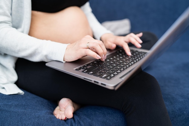 A pregnant woman wearing sports clothes sits on the couch in the living room and texting an email to