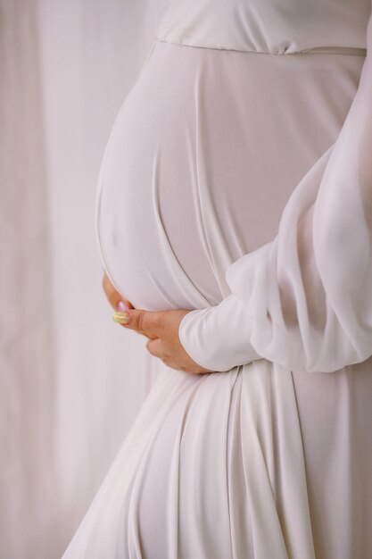 Photo pregnant woman in white dress holding her belly on white background space for text