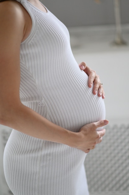 Pregnant woman in white sweater holding her belly