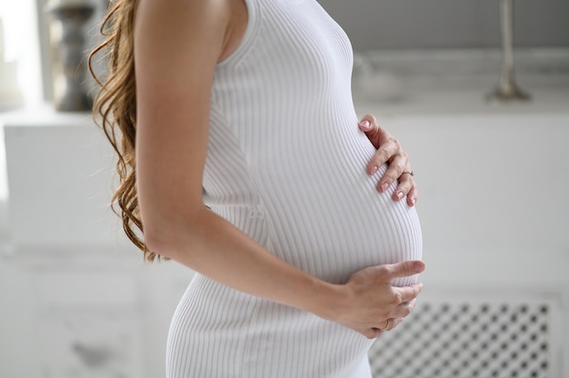 Pregnant woman in white sweater holding her belly