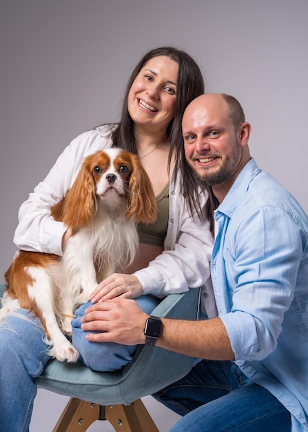 A pregnant woman with a bare belly sits in a chair holds a cocker spaniel and hugs her husband