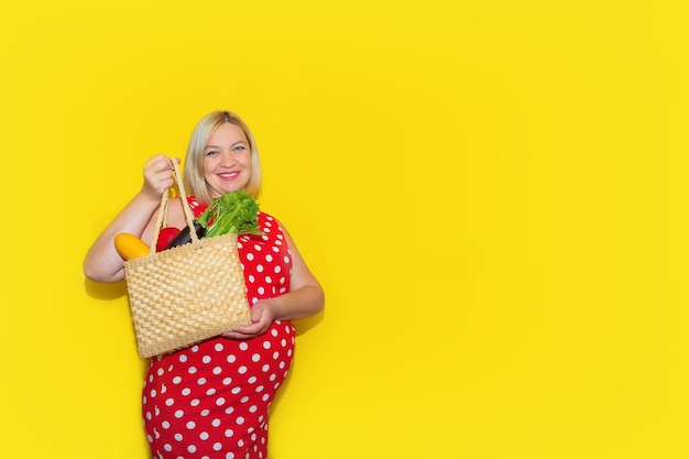 Pregnant woman with a basket of vegetables and fruits on a yellow background with copy space