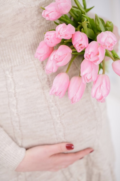 Pregnant woman with bouquet of tulips touch bell. close up