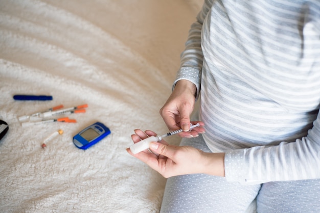 Pregnant woman with insulin syringe in home on bed. Pregnant diabetes concept.