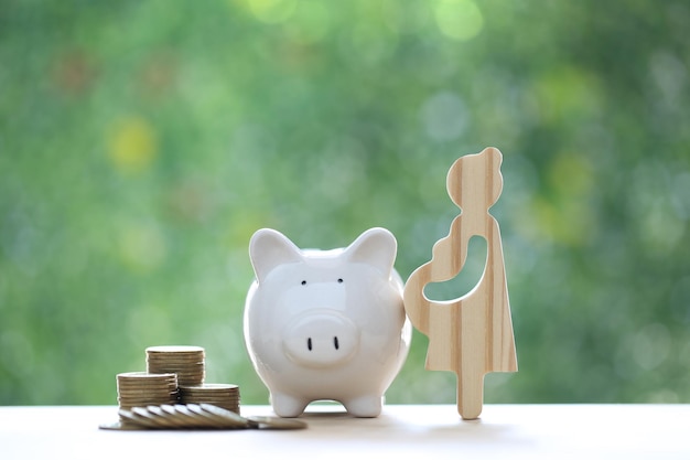 Pregnant woman with piggy bank and gold coin money on natural green background