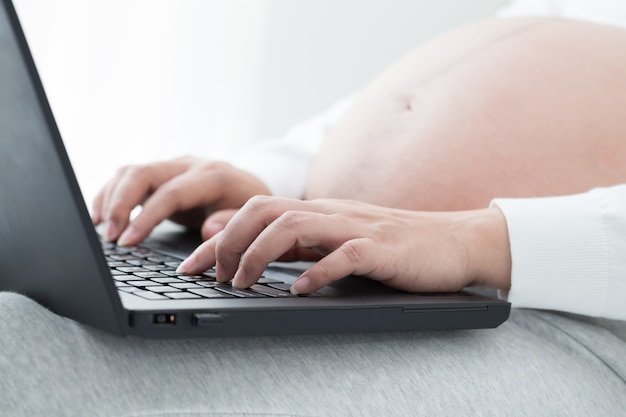 Pregnant women hand typing on keyboard on notebook to searching newborn baby items for preparing parenthood