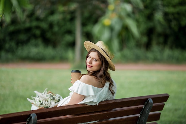 Pregnant young beautiful woman drinks cappuccino in the park