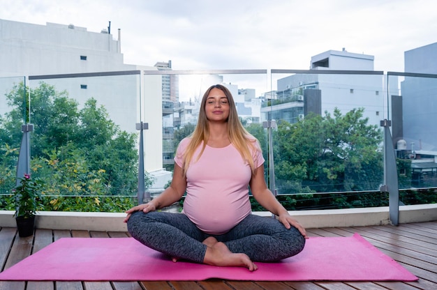 Pregnant young woman at home practicing yoga and meditation on a pink mat