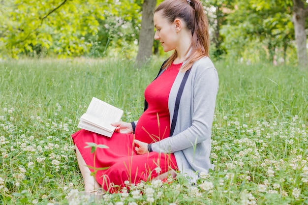 A pregnant young woman is reading a book in a park sitting on the grass Soft focus