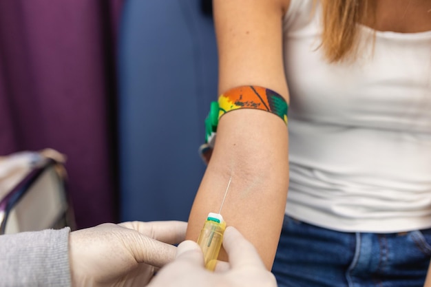 Preparation for blood test with pretty young woman by female doctor medical uniform on the table in white bright room Nurse pierces the patient's arm vein with needle blank tube