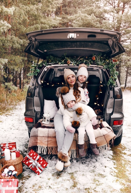 Preparation for Christmas. Two little girls with their mother have fun playing in the trunk of a car