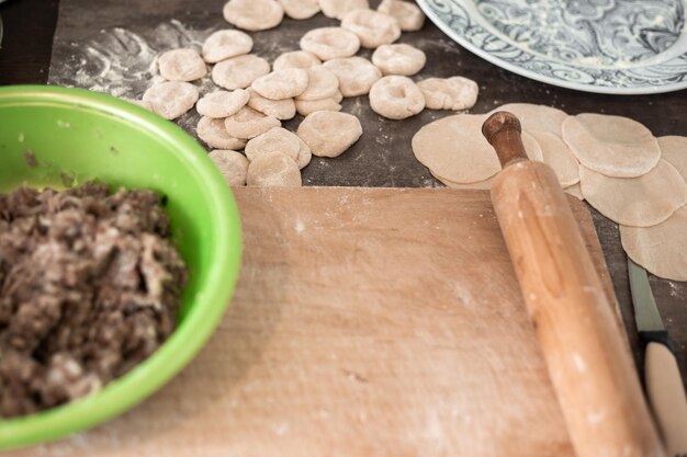 Preparation of dumplings meat filling in a cup dough dumplings and a board with a rolling pin