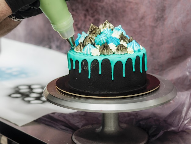 Preparation of frosted black painted cup cake with blue turquoise dripping