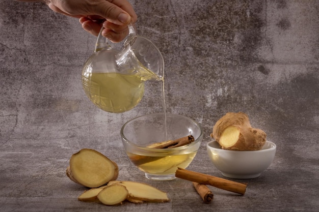 preparation of a ginger and cinnamon infusion with fresh produce natural roots and cinnamon stick served in a pitcher and a cup