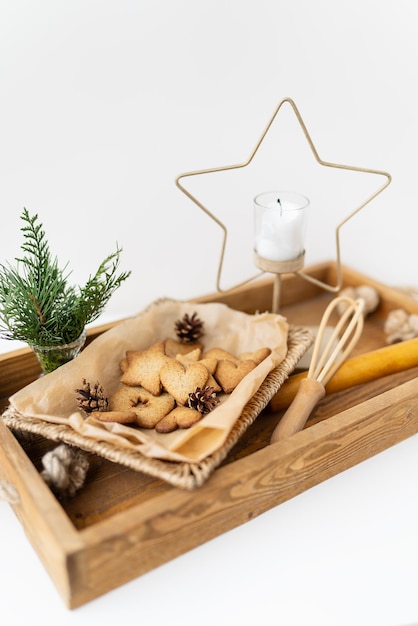 Preparation of gingerbread cookies different gingerbread cookies of different shapes lie on a wooden tray along with a star candle a whisk and a bouquet of arborvitae Holiday concept