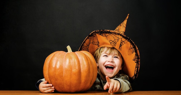 Photo preparation halloween holiday happy child in witch hat with halloween pumpkin pointing finger at you