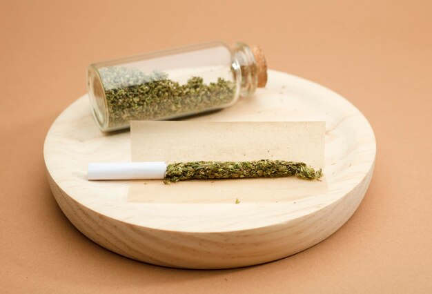 preparation of marijuana cigarette with glass bottle on wood brown background