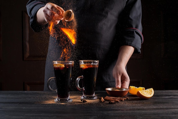 Preparation of mulled wine to serve, in a restaurant. Mulled wine in the preparation of the chef's bar. The hands of the chef on a dark black background. Burning mulled wine with sparks.