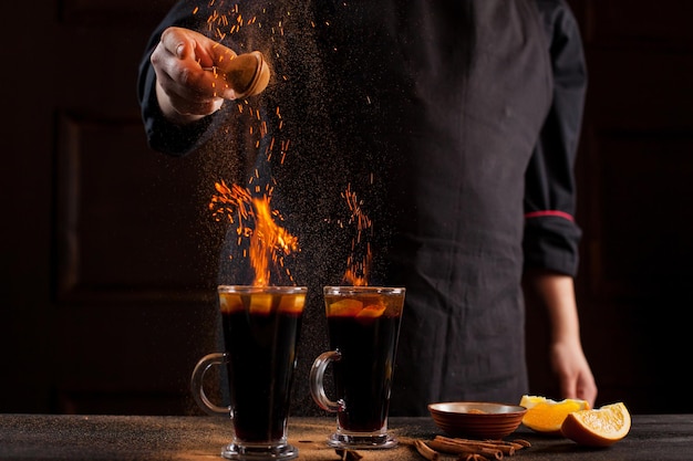 Preparation of mulled wine to serve, in a restaurant. Mulled wine in the preparation of the chef's bar. The hands of the chef on a dark black background. Burning mulled wine with sparks.