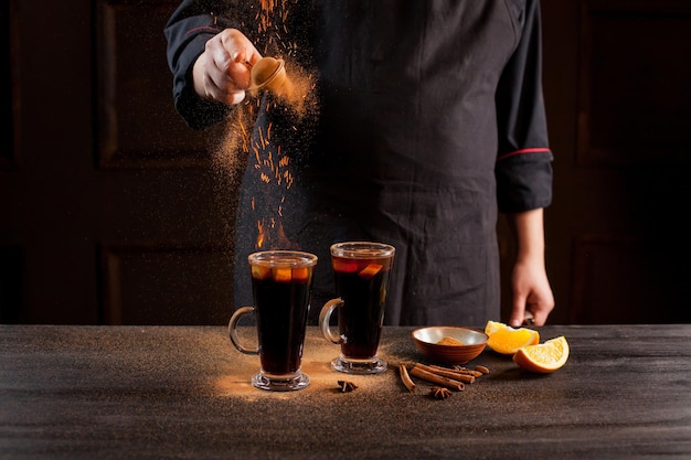 Preparation of mulled wine to serve, in a restaurant. Mulled wine in the preparation of the chef's bar. The hands of the chef on a dark black background. Burning mulled wine with sparks.