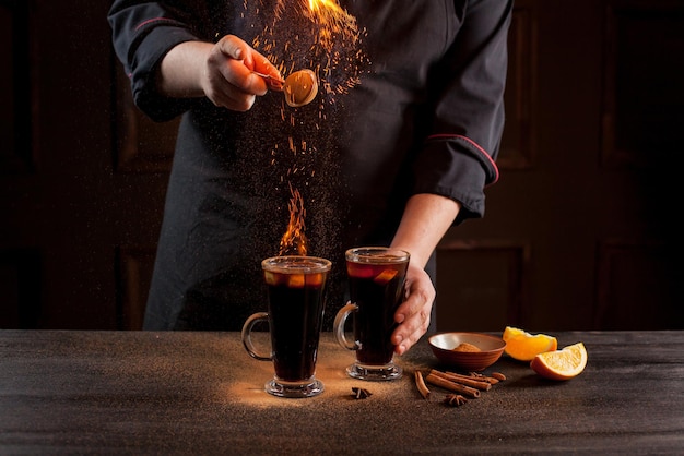 Preparation of mulled wine to serve, in a restaurant. Mulled wine in the preparation of the chef's bar. The hands of the chef on a dark black background. Burning mulled wine with sparks.