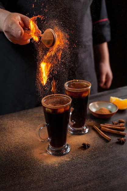 Preparation of mulled wine to serve, in a restaurant. Mulled wine in the preparation of the chef's bar. The hands of the chef on a dark black background. Burning mulled wine with sparks.