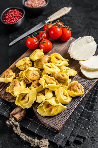 Preparation of raw ravioli with Mozzarella cheese and Tomato. Black background. Top view.