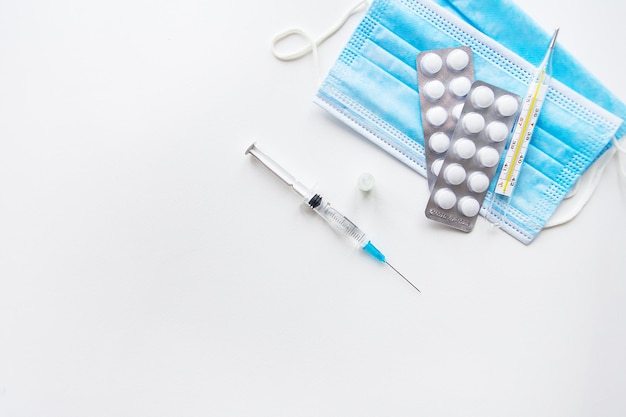 Preparation for vaccination against covid-19. Syringe, vaccine, pills, medical mask on a white table. View from above.