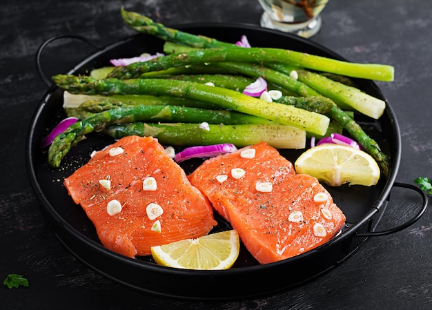 Prepared for baking salmon with asparagus lemon slices and spices on dark table