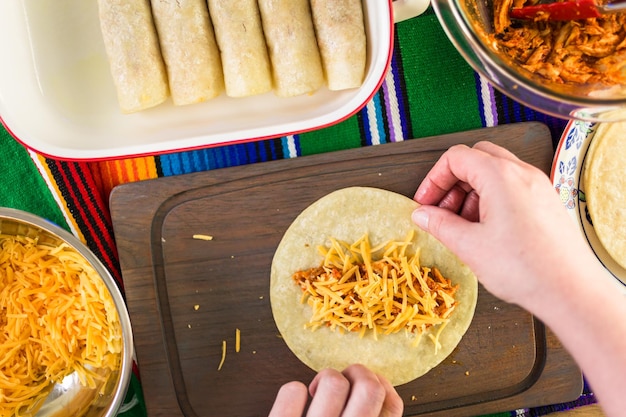 Preparing chicken enchiladas with cheddar cheese and sauce.