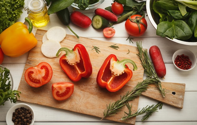 Preparing fresh vegetable salad at kitchen table top view. Cutting red ripe pepper and tomato on wooden board, copy space