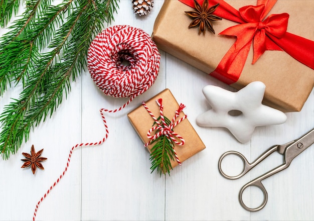 Preparing for the holidays, wrapping gifts, top view with copy space.  gift boxes in craft paper, striped rope, festive cookies and a branch of a Christmas tree on a white wooden table.