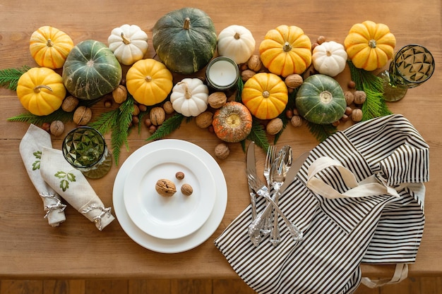 Preparing for Thanksgiving table set. Plate, wine glass, cutlery and a self-paper on a wooden table. Table decoration of pumpkins, nuts, apron, candles and juniper with copy space.