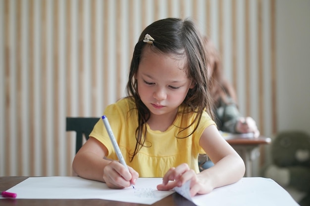 Preschool Girl Kid Drawing With Color Pencil On White Paper On Table In Classroom With Friends