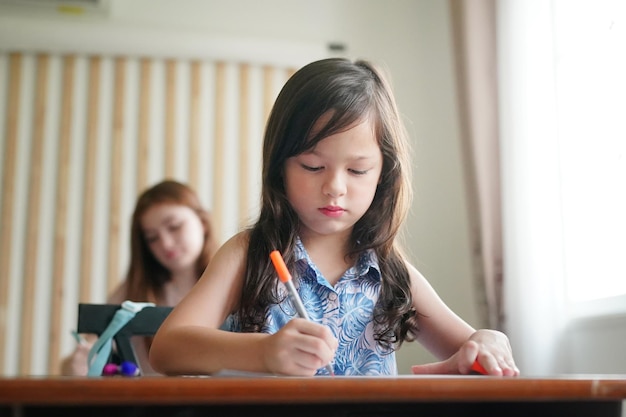 Preschool Girl Kid Drawing With Color Pencil On White Paper On Table In Classroom With Friends