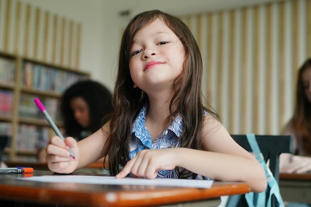 Preschool Girl Kid Drawing With Color Pencil On White Paper On Table In Classroom With Friends